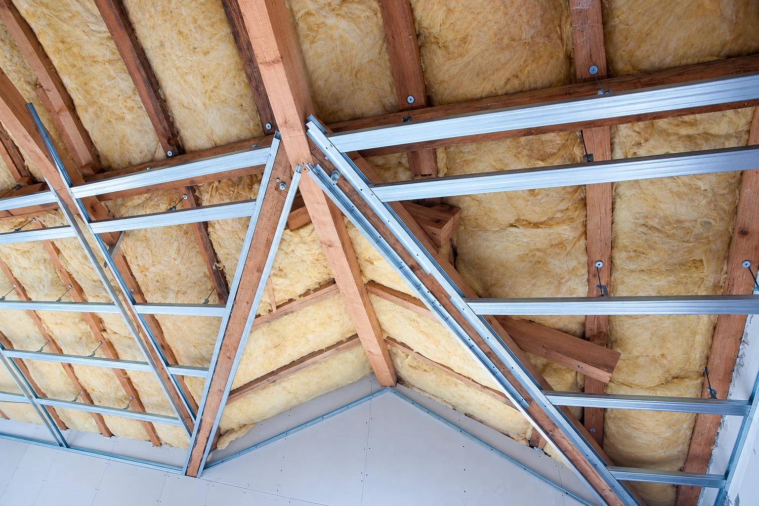 Yellow insulation fills the roof rafters above exposed silver metal ceiling channels and unfinished drywall.