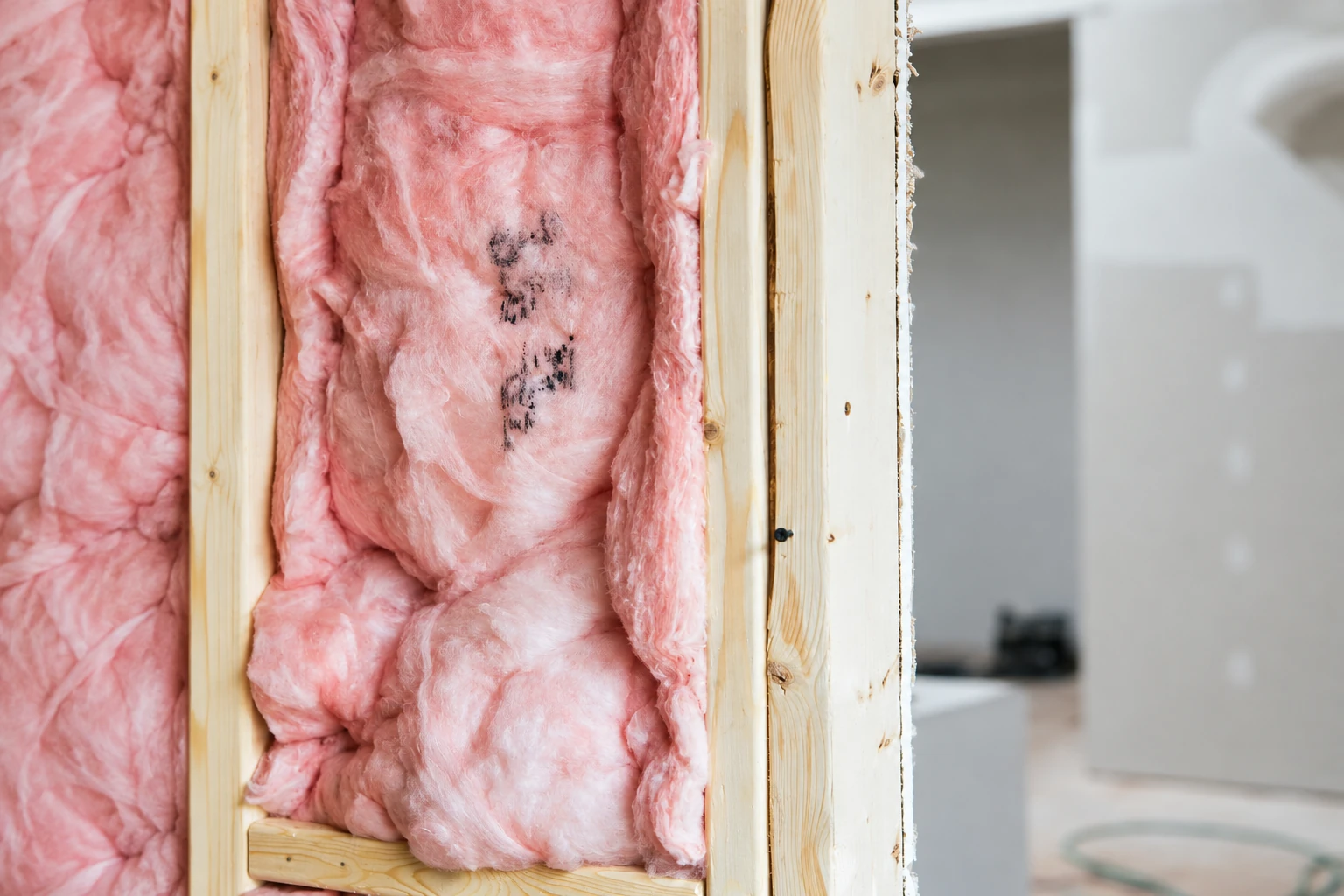 Pink fiberglass batts fill the open spaces between wooden wall studs.